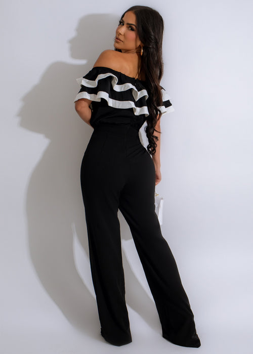  Full-length image of a woman wearing a black jumpsuit with a deep V-neck and strappy heels