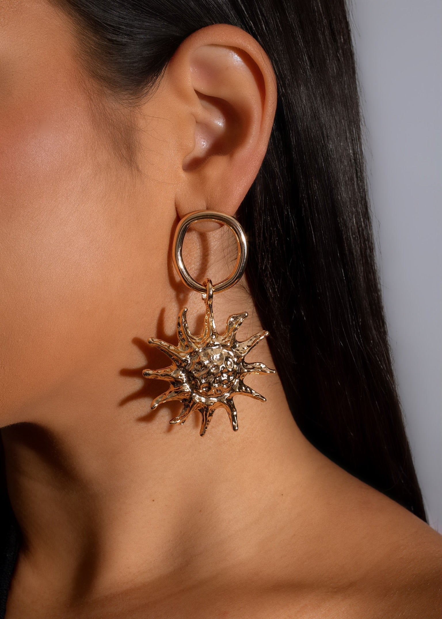 A pair of gold sunshine shaped earrings, featuring a radiant design