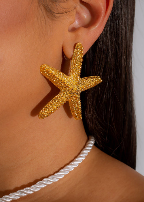 My Tiny Starfish Earrings Gold shimmering in the sunlight on a woman's ear, adding a touch of elegance and beachy vibes to any outfit 