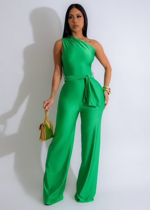 Close-up of the soft green ruched jumpsuit with tie waist and square neckline on a model posing in a field of flowers