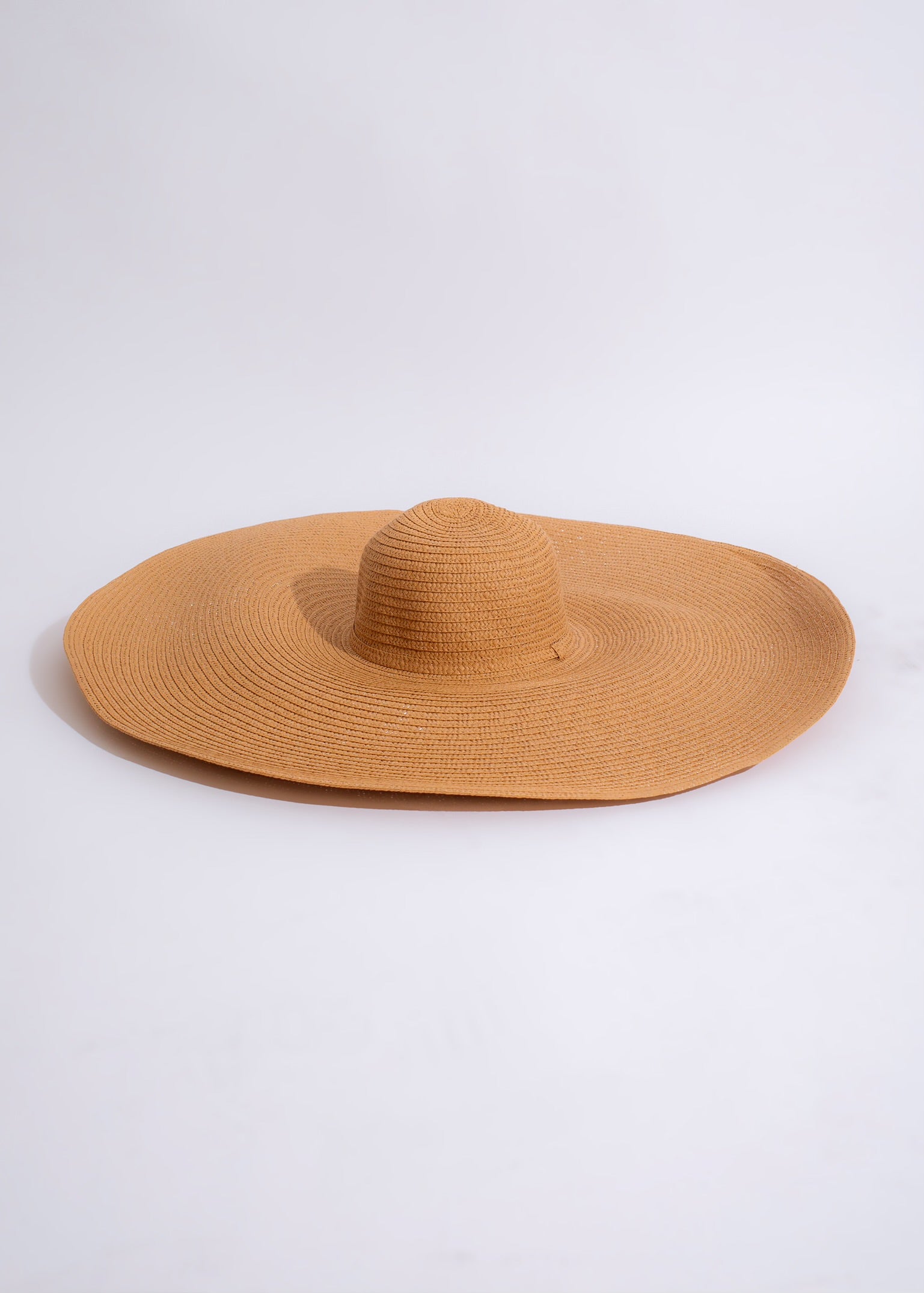 Adventures In The Sand Hat Brown on a sunny beach with waves crashing in the background and a person wearing the hat, enjoying the scenery